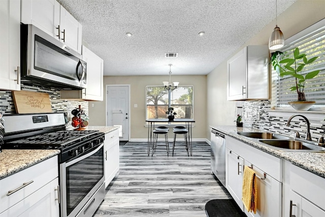 kitchen with a sink, light wood-style floors, appliances with stainless steel finishes, and white cabinetry