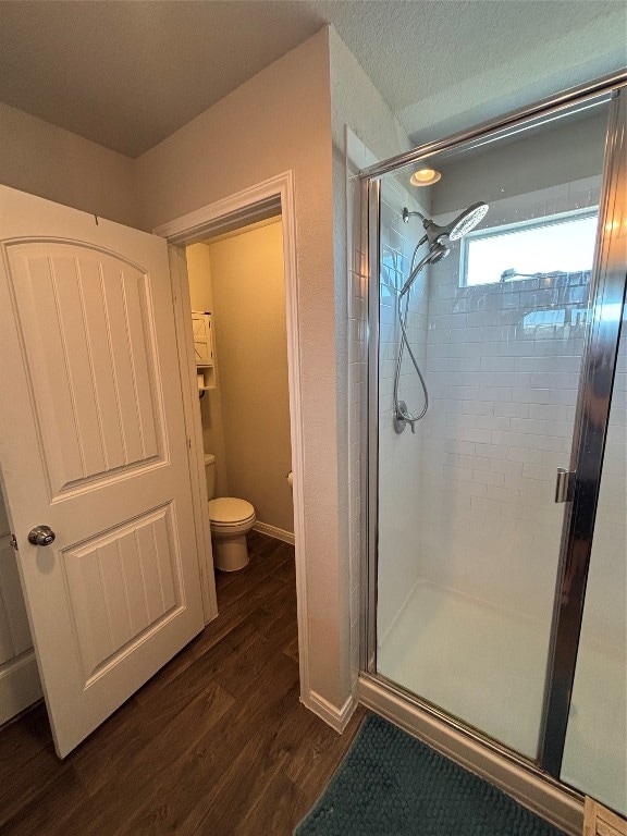 bathroom featuring a shower with door, hardwood / wood-style flooring, a textured ceiling, and toilet