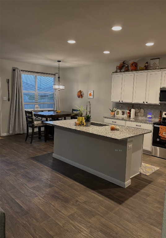 kitchen featuring a center island with sink, appliances with stainless steel finishes, hanging light fixtures, and dark wood-type flooring