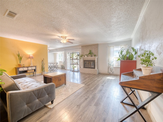 living room with a fireplace, crown molding, a wealth of natural light, and light hardwood / wood-style floors