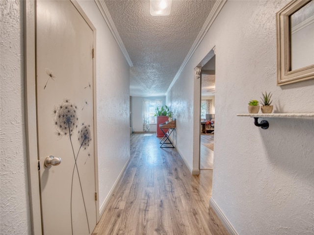 hallway with ornamental molding, a textured ceiling, and light hardwood / wood-style flooring