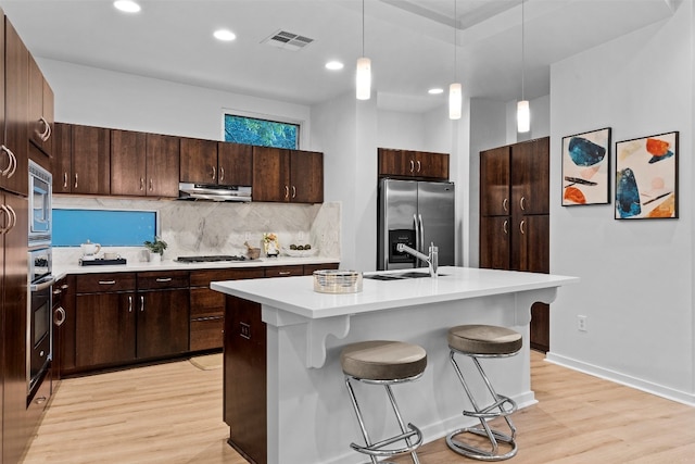 kitchen featuring hanging light fixtures, a kitchen island with sink, light hardwood / wood-style floors, stainless steel appliances, and ventilation hood