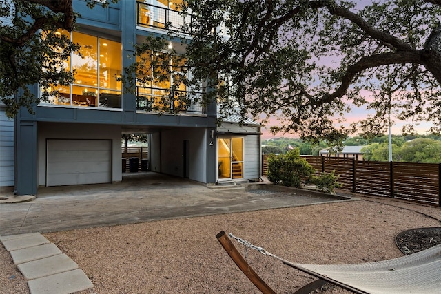 back house at dusk with a garage and a balcony