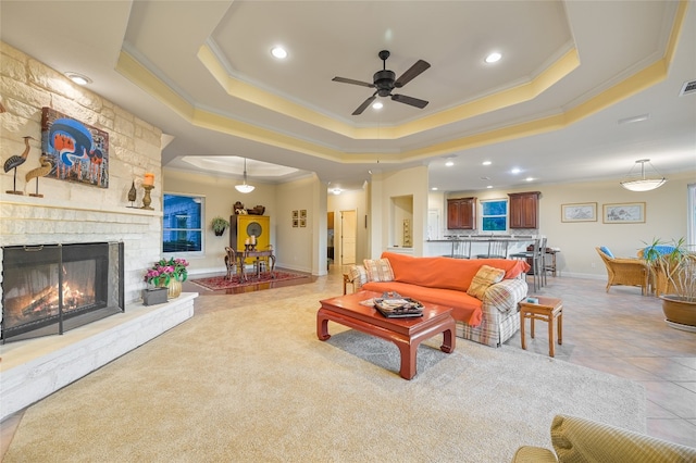 living area featuring light tile patterned floors, a fireplace, a raised ceiling, and ornamental molding