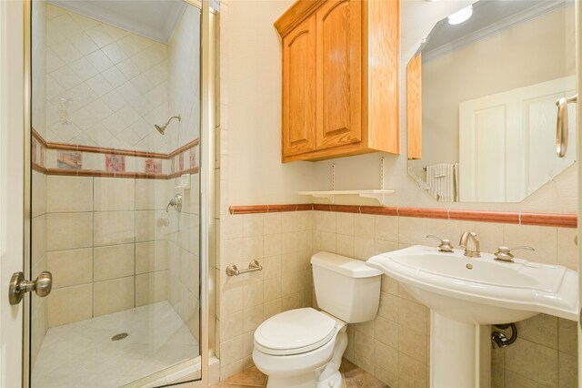 bathroom featuring tile walls, crown molding, a shower with door, and toilet