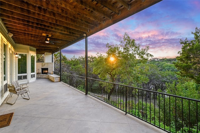 patio terrace at dusk featuring an outdoor stone fireplace and a ceiling fan