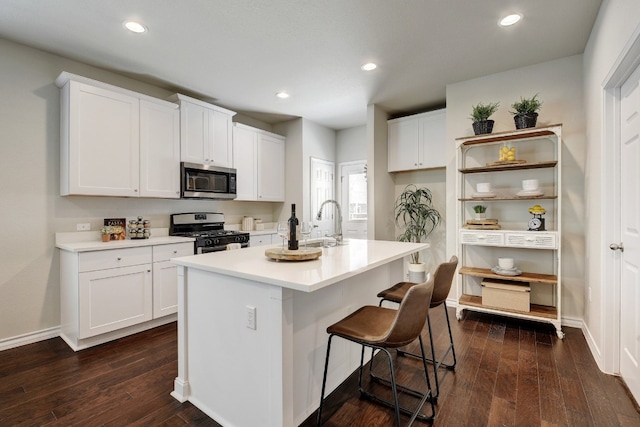 kitchen with a center island with sink, white cabinets, dark hardwood / wood-style floors, and appliances with stainless steel finishes