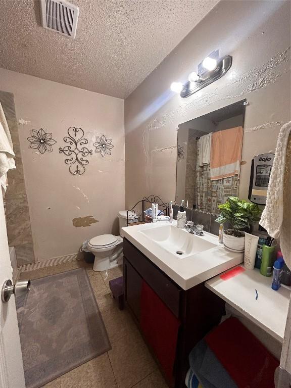 bathroom featuring vanity, toilet, tile patterned flooring, and a textured ceiling