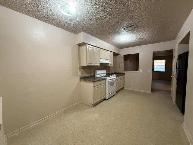 kitchen featuring white range with gas cooktop, tasteful backsplash, black refrigerator, and a textured ceiling