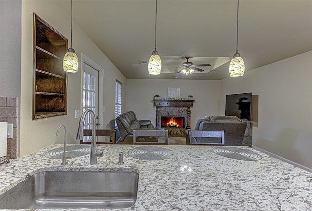 kitchen featuring hanging light fixtures, sink, light stone counters, and ceiling fan