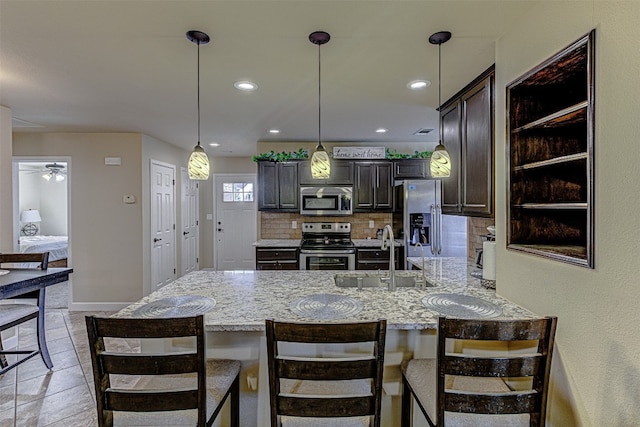 kitchen with ceiling fan, sink, a breakfast bar area, appliances with stainless steel finishes, and backsplash