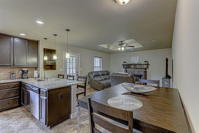 kitchen featuring ceiling fan, tasteful backsplash, decorative light fixtures, sink, and light stone counters