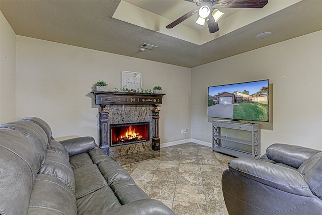 living room featuring ceiling fan, a stone fireplace, and a textured ceiling