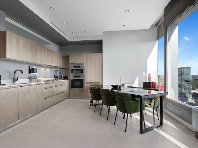 kitchen featuring light brown cabinetry, stainless steel double oven, sink, and a healthy amount of sunlight