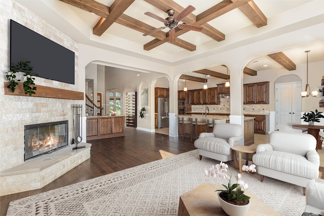 living room with coffered ceiling, ceiling fan, beam ceiling, dark hardwood / wood-style floors, and a stone fireplace