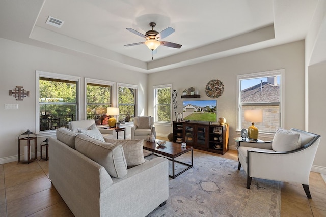 tiled living room featuring ceiling fan and a tray ceiling