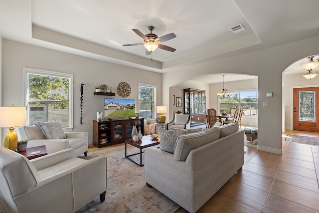 tiled living room featuring a wealth of natural light, a raised ceiling, and ceiling fan with notable chandelier