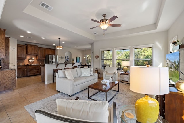 living room featuring ceiling fan, a tray ceiling, and light tile patterned floors