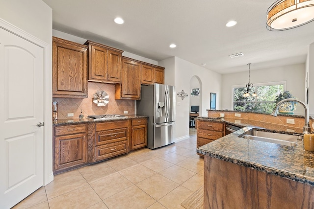 kitchen featuring stainless steel appliances, dark stone counters, hanging light fixtures, sink, and light tile patterned floors