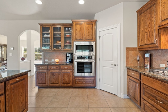 kitchen featuring stainless steel appliances, dark stone counters, tasteful backsplash, and light tile patterned floors