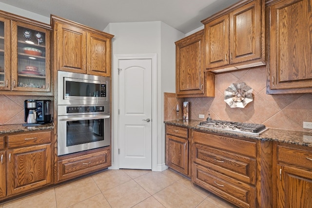 kitchen featuring appliances with stainless steel finishes, dark stone counters, tasteful backsplash, and light tile patterned floors