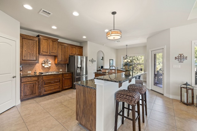 kitchen with dark stone countertops, appliances with stainless steel finishes, an island with sink, and light tile patterned flooring