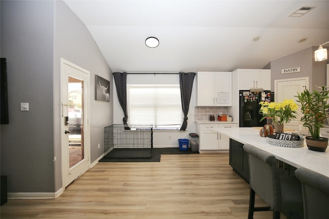 kitchen featuring black fridge, light hardwood / wood-style flooring, vaulted ceiling, and white cabinets