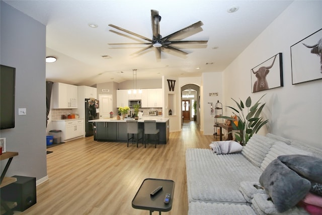 living room featuring light wood-type flooring, ceiling fan, and vaulted ceiling