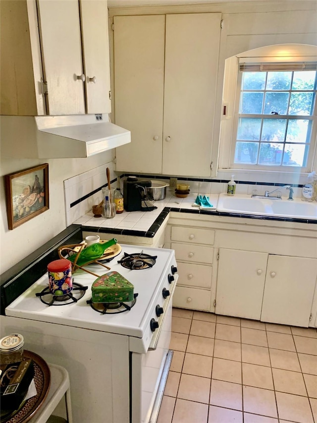 kitchen featuring sink, white gas stove, tile countertops, light tile patterned floors, and white cabinets