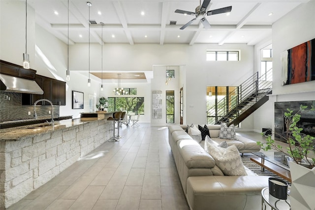 living room featuring ceiling fan with notable chandelier, beam ceiling, a towering ceiling, and sink