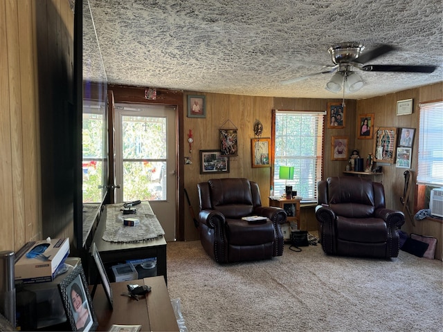 carpeted living room featuring ceiling fan and wooden walls