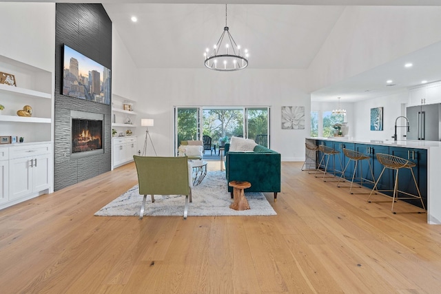 living room with high vaulted ceiling, a tiled fireplace, built in shelves, light wood-type flooring, and a chandelier