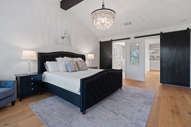 bedroom with ensuite bath, a barn door, light wood-type flooring, and a chandelier