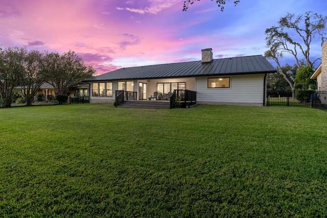 back house at dusk with a lawn and a wooden deck