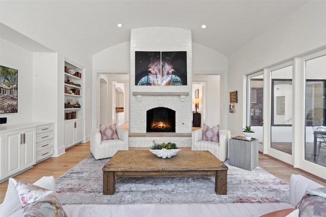 living room with lofted ceiling, built in features, a fireplace, and light wood-type flooring