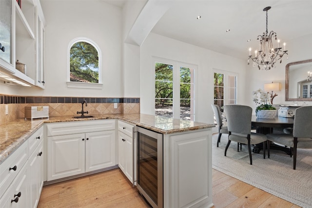 kitchen with light stone countertops, light wood-type flooring, kitchen peninsula, white cabinetry, and beverage cooler