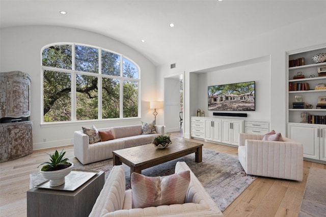 living room featuring vaulted ceiling, light hardwood / wood-style flooring, and built in shelves