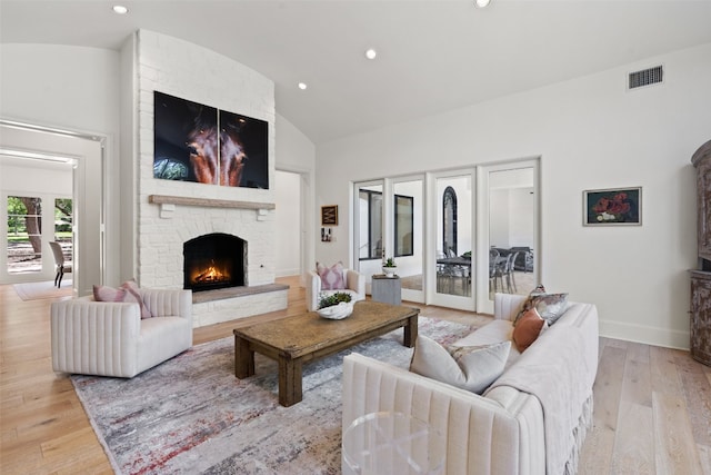 living room featuring french doors, light hardwood / wood-style floors, a stone fireplace, and vaulted ceiling