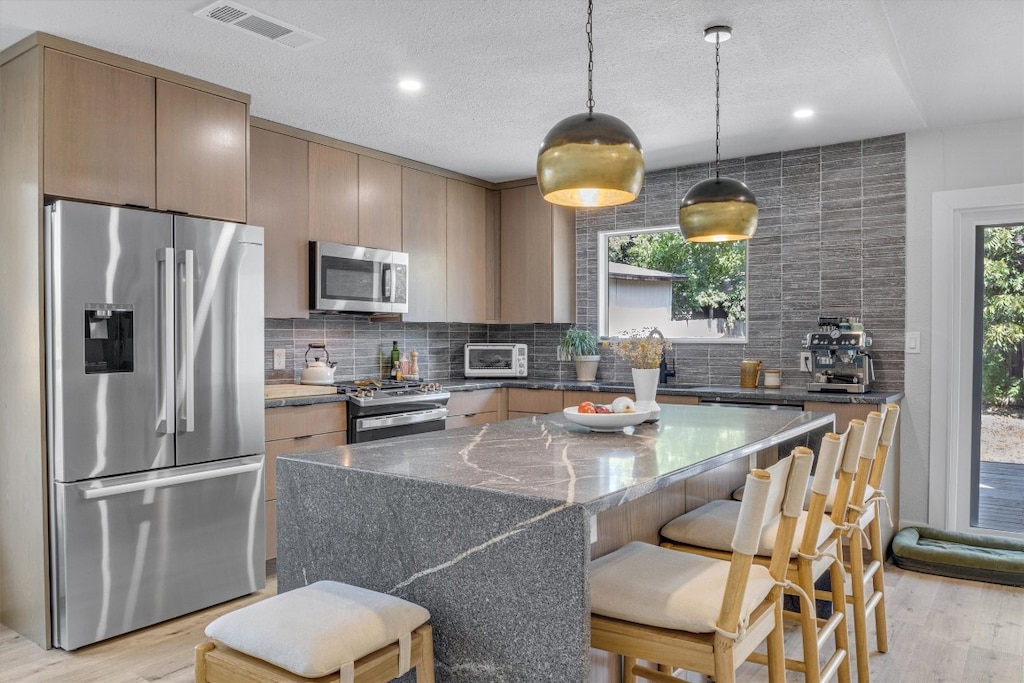 kitchen featuring a kitchen island, backsplash, stainless steel appliances, and light hardwood / wood-style flooring