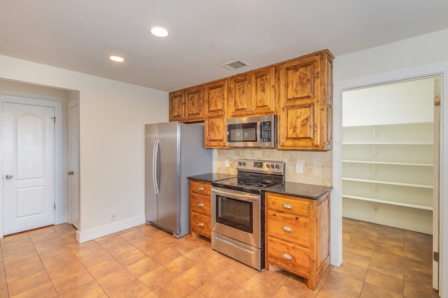 kitchen with dark stone countertops, appliances with stainless steel finishes, light tile patterned floors, and decorative backsplash