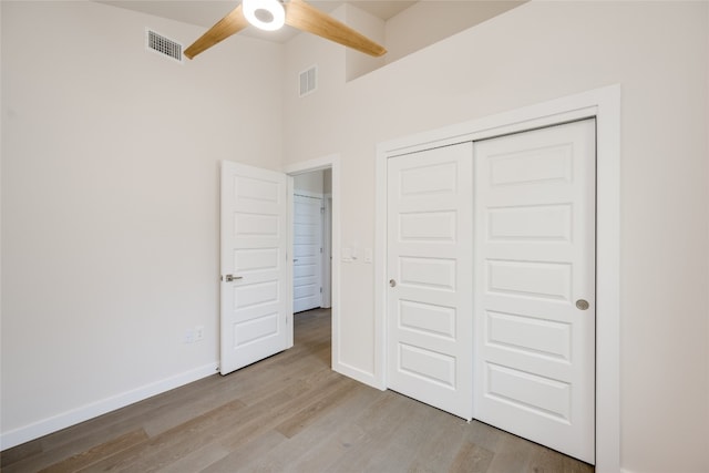 unfurnished bedroom with a high ceiling, ceiling fan, a closet, and light hardwood / wood-style flooring