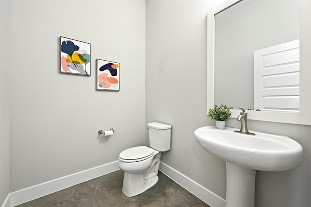 bathroom with toilet, concrete flooring, and sink