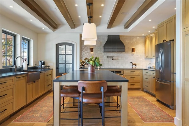 kitchen featuring stainless steel refrigerator with ice dispenser, custom exhaust hood, sink, beam ceiling, and a breakfast bar area