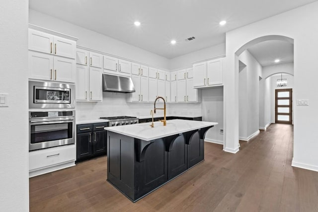 kitchen featuring a kitchen island with sink, white cabinets, dark hardwood / wood-style floors, and appliances with stainless steel finishes