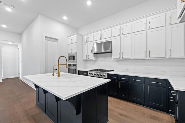 kitchen with white cabinetry, sink, stainless steel appliances, wood-type flooring, and a center island with sink