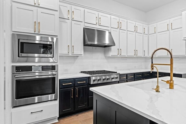 kitchen with light stone countertops, ventilation hood, stainless steel appliances, and white cabinetry