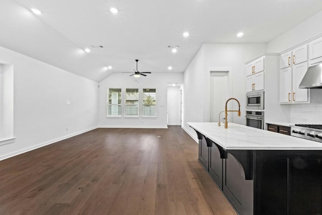 kitchen with stainless steel appliances, dark wood-type flooring, white cabinets, lofted ceiling, and an island with sink