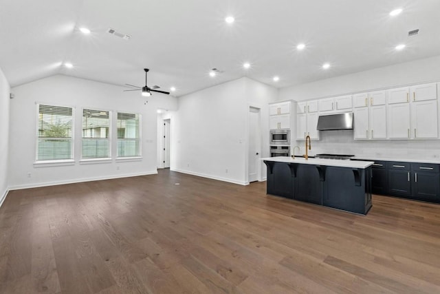 kitchen with white cabinets, dark hardwood / wood-style floors, an island with sink, a kitchen bar, and stainless steel appliances