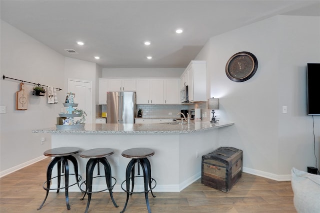 kitchen with light hardwood / wood-style floors, stainless steel appliances, kitchen peninsula, and white cabinetry