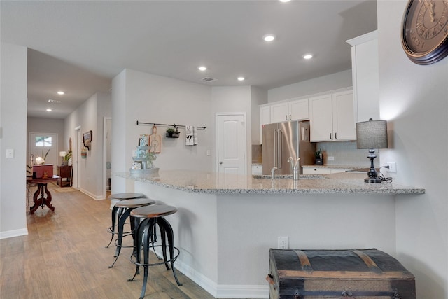 kitchen with high quality fridge, light hardwood / wood-style flooring, sink, kitchen peninsula, and white cabinetry